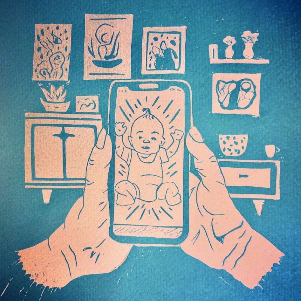 A linocut image printed in blue ink. The image shows two hands holding up a phone with a baby on the screen. Behind the phone are pictures and furniture showing the person is in their living room.