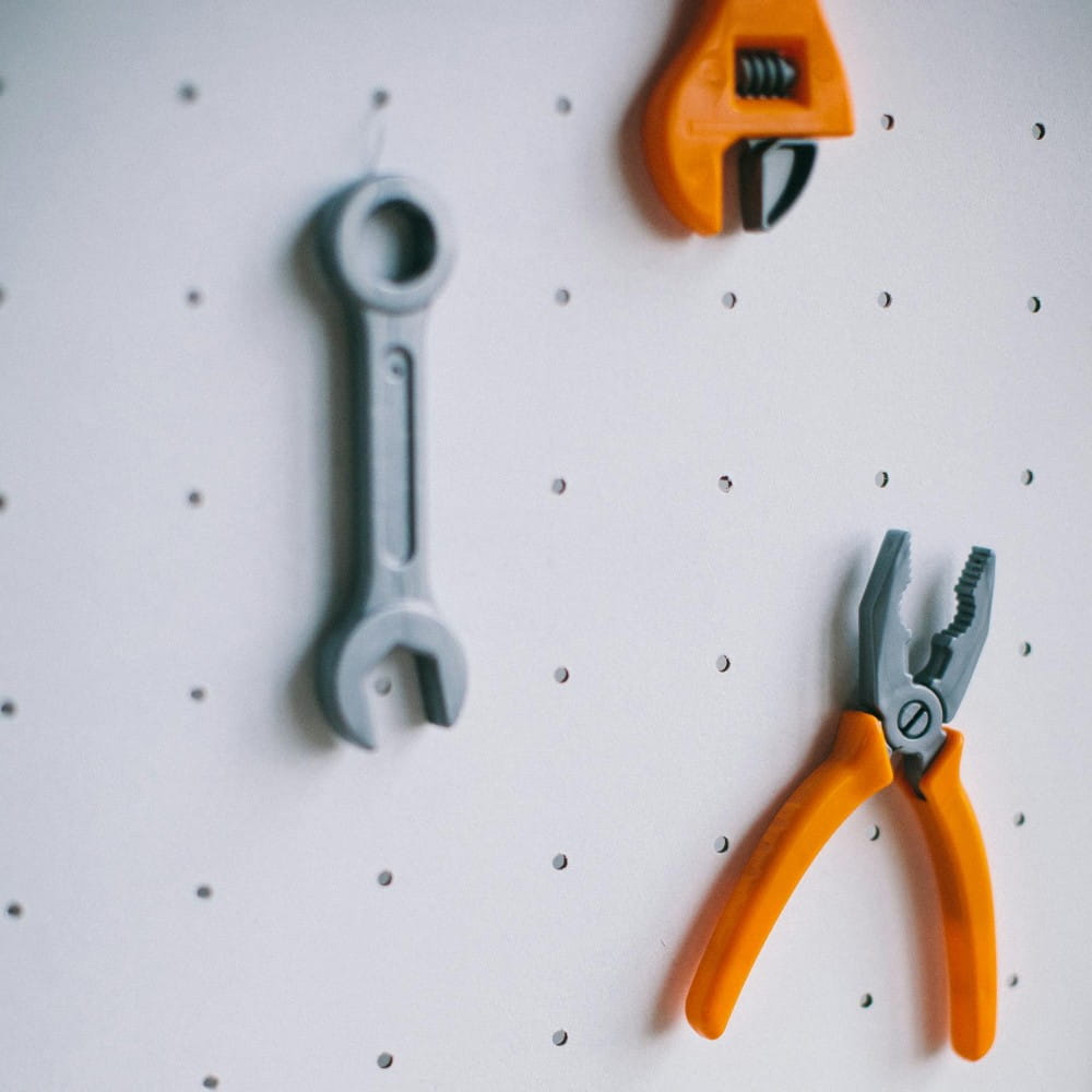 Children's toy versions of a spanner, pliers and a wrench hanging up on a peg board.