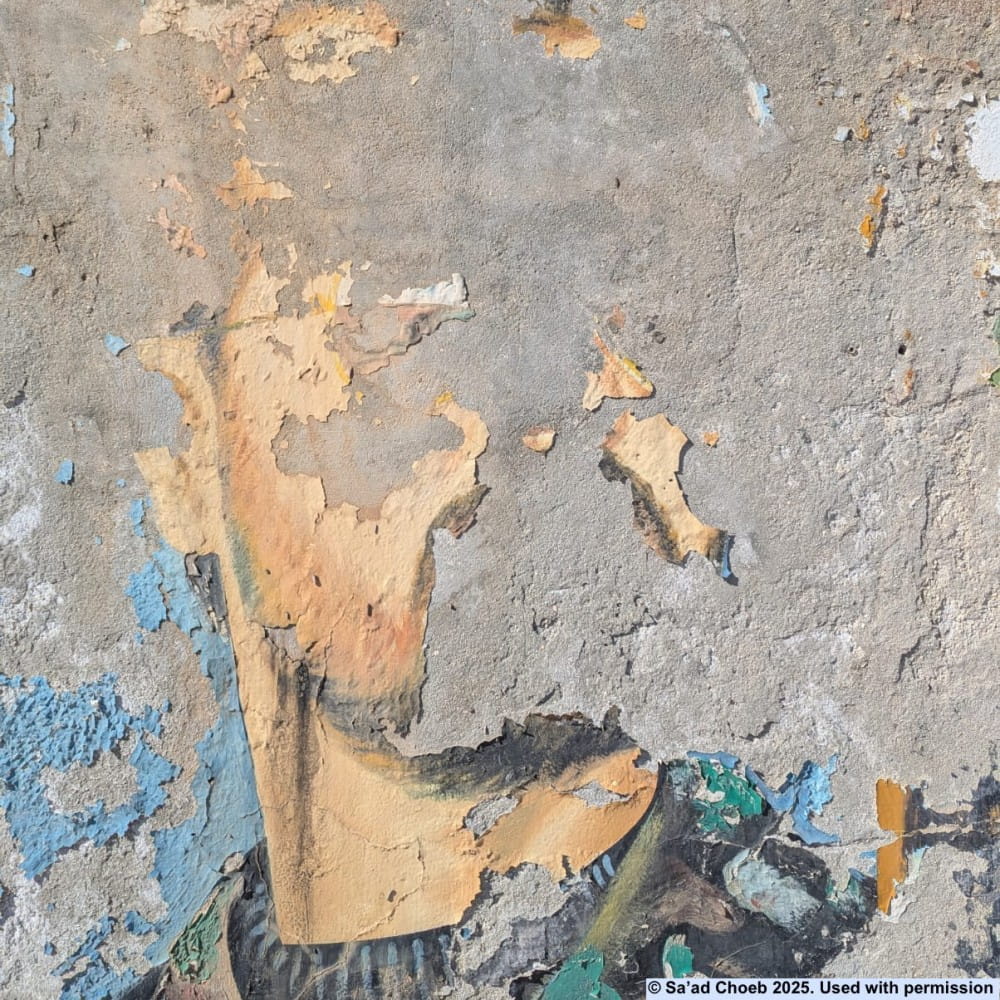 A wall painting of Bassel al-Assad in Syria. Most of the paint has flaked off, leaving his cheek and neck and some military uniform.