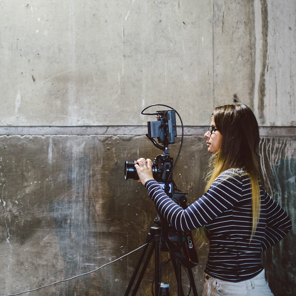 Female student facing to the left adjusting the lens of a film camera on a tripod