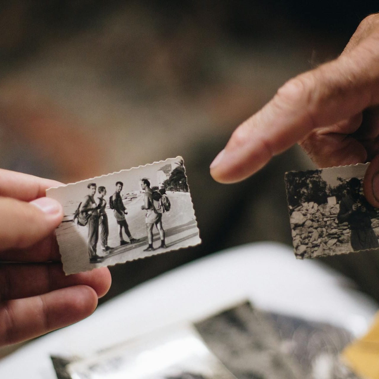 A person out of shot is holding a small black and white photo of four people. Another person out of shot is pointing a finger towards the photo.