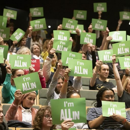 People in an audience holding up a sign which says I'm All In - a project from Eastlight Community Homes