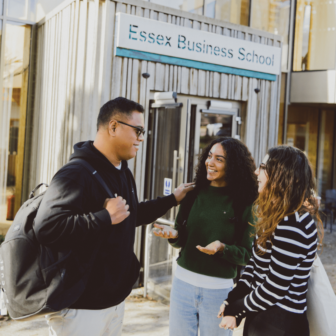 3 students laughing and chatting in front of a sign that says 'Essex Business School'