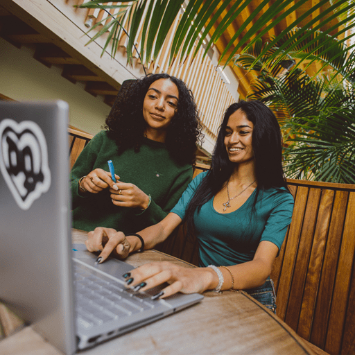 Two female students smiling and chatting over a laptop