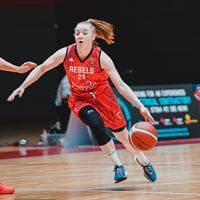 Essex Rebels Megan Haines dribbles a ball on a basketball court, she is wearing the home kit and is edging round a defender