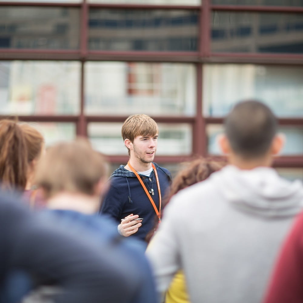 A man stands in front of a crowd talking to them