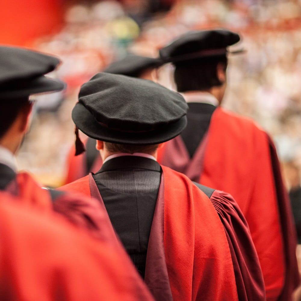 A shot of the back of three people standing in a line wearing red and black graduation robes and hats.