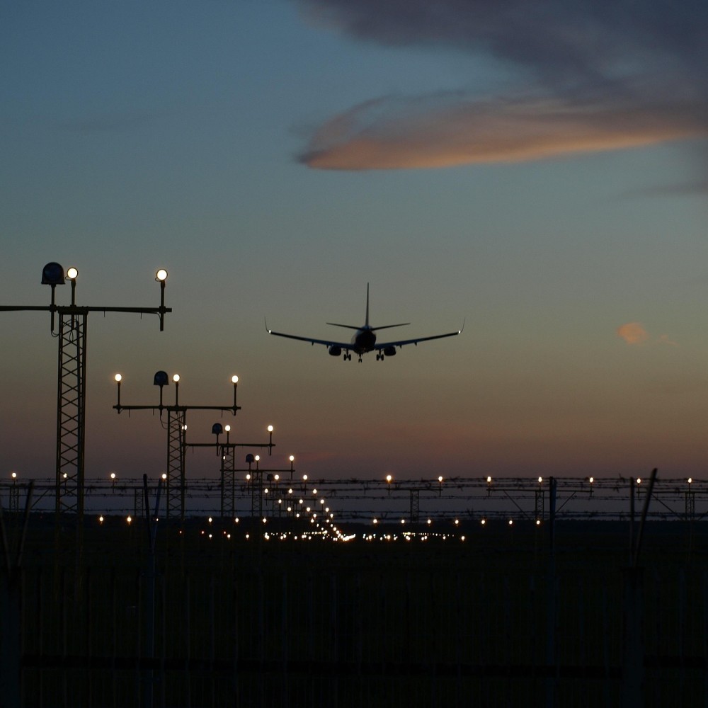 A passenger plane coming in to land on a runway at sunset, with a row of guiding lights on the left.
