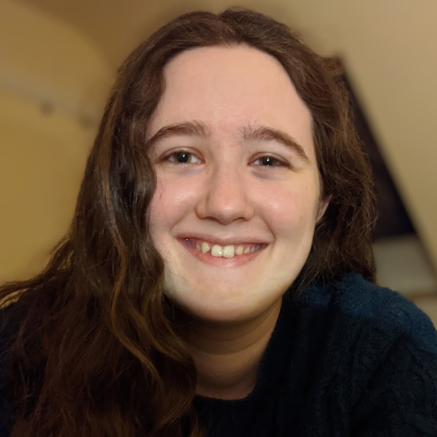 CSEE graduate Ayla Sensibar, with long brown hair and a dark top, smiling at the camera.