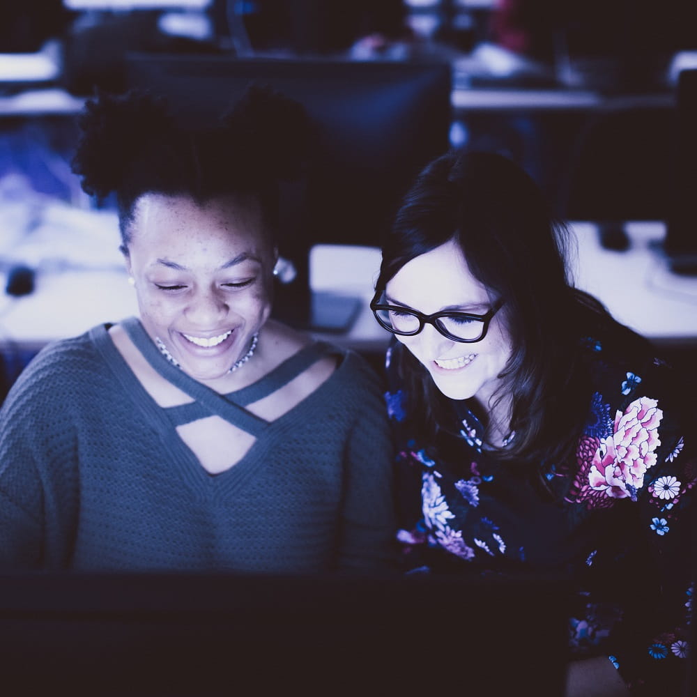 Two women laughing as they look at a computer screen