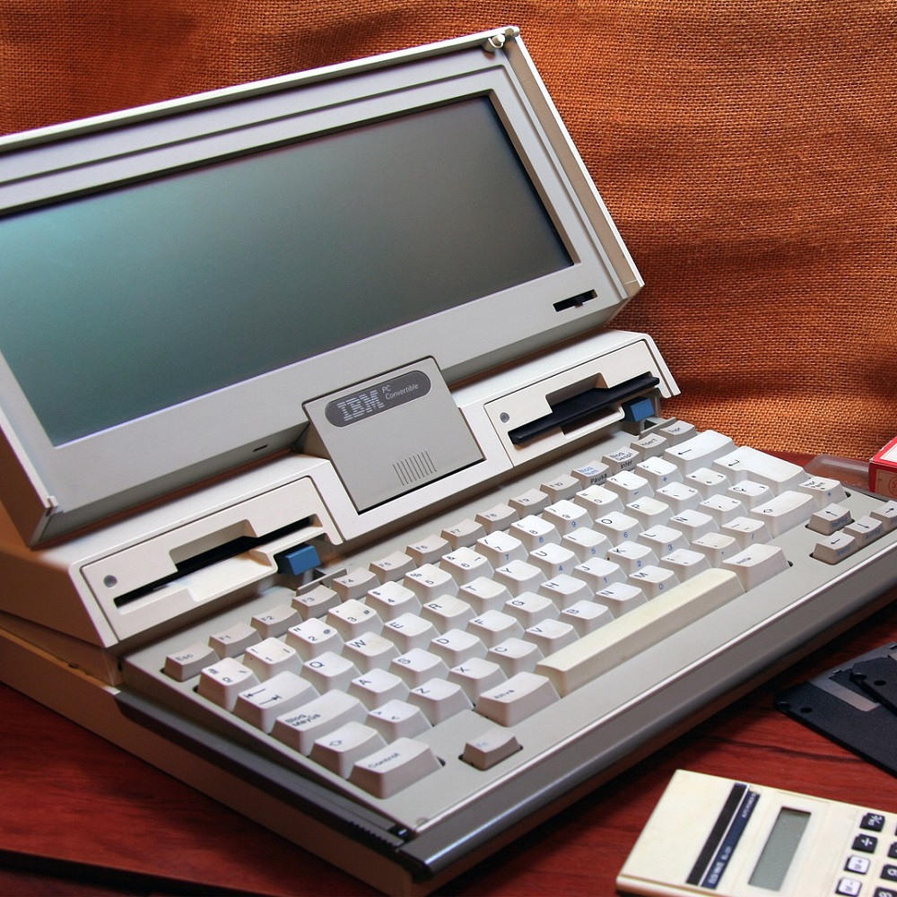A very old IBM computer in grey, with a calculator visible in front of the keyboard.