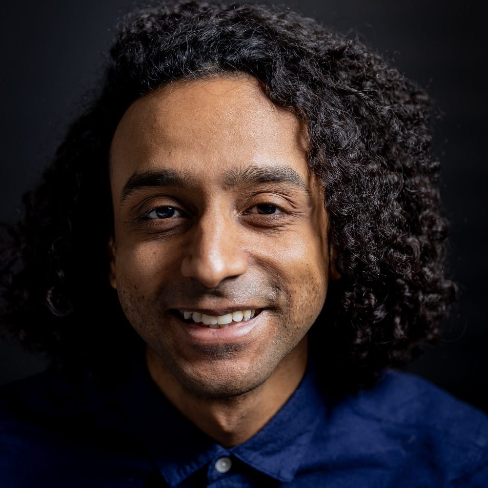CSEE graduate Yunis Osman smiling at the camera, wearing a blue shirt with a black background behind him.