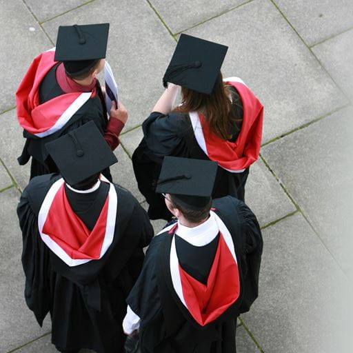 A top-down photo of a group of four people wearing black graduation robes trimmed with red and white, and mortarboards on their heads.