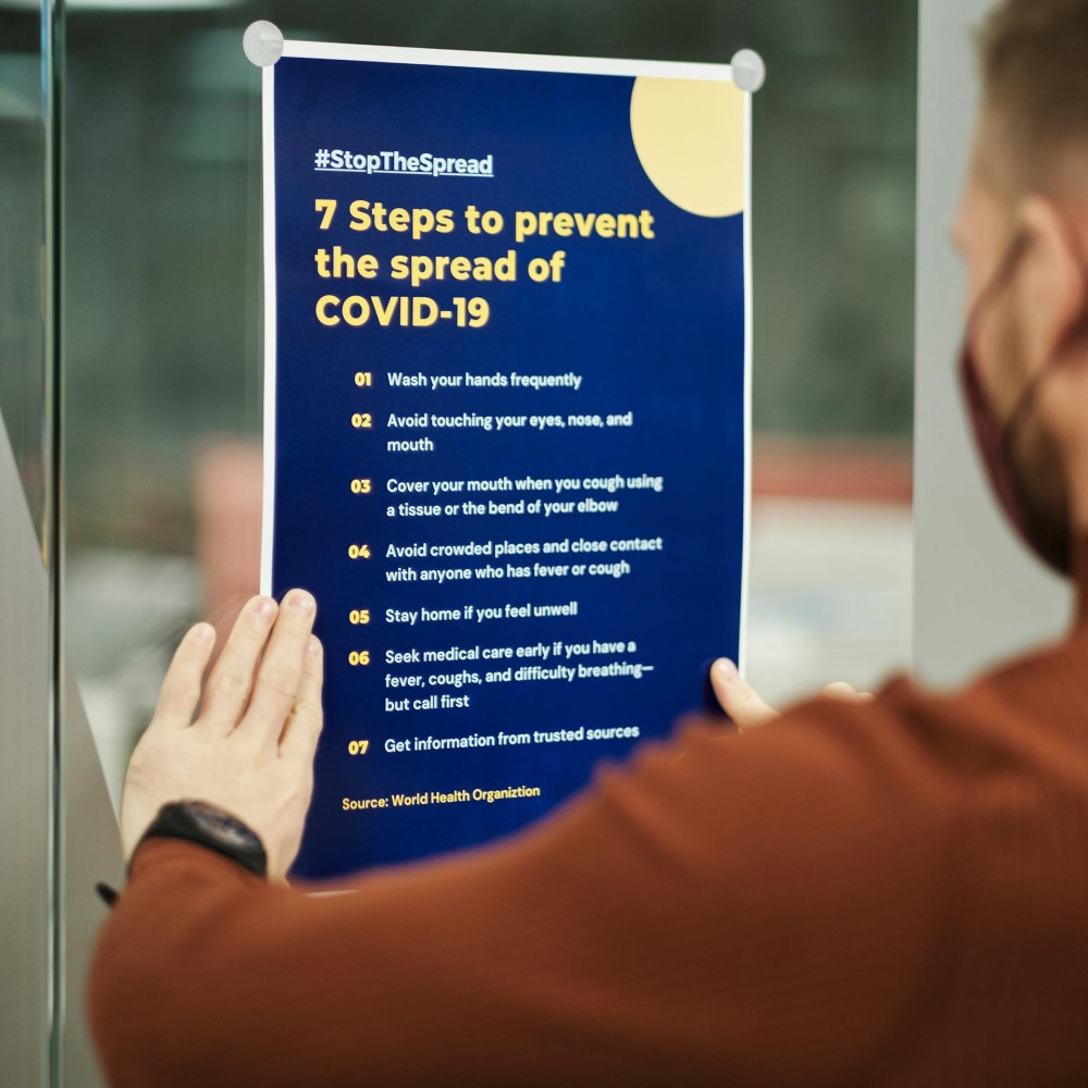 A person wearing a brown top sticking up a poster about steps to prevent the spread of COVID-19.
