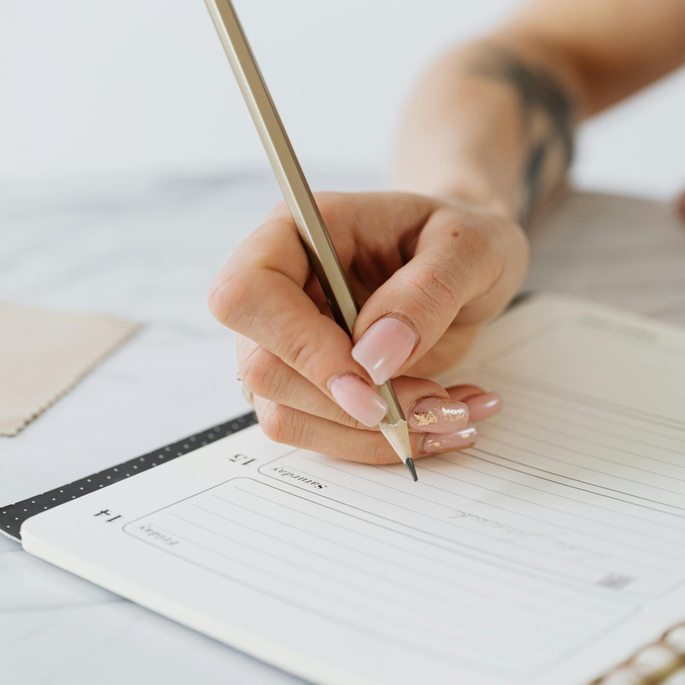 A hand holding a pencil, poised to write in a weekly diary.