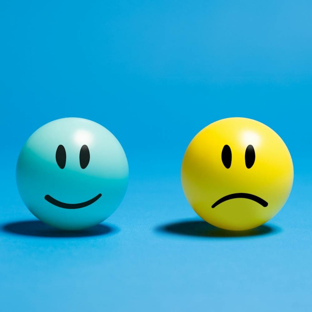 A blue ball with a smiling face and a yellow ball with a sad face, side by side with a blue background.