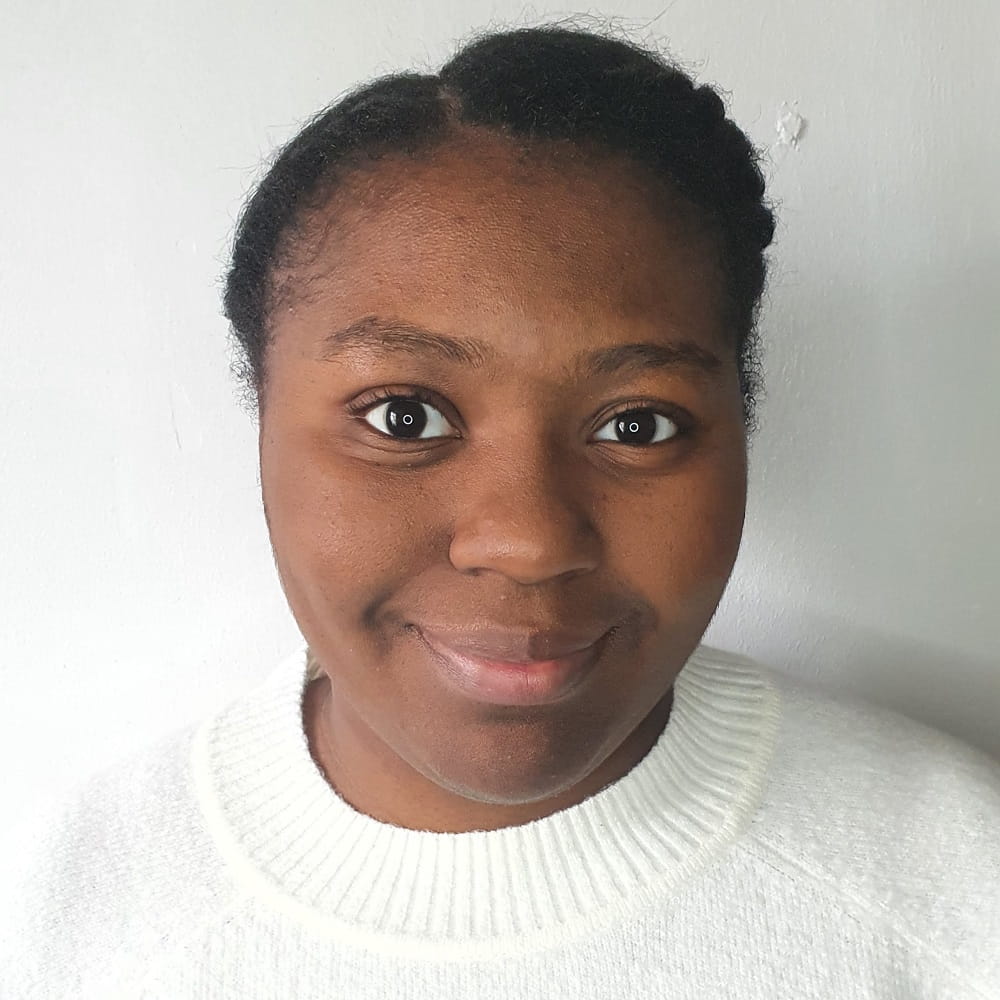 Psychology graduate Janelle Chisholm, a Black woman smiling at the camera, wearing a white top and standing in front of a blank background.
