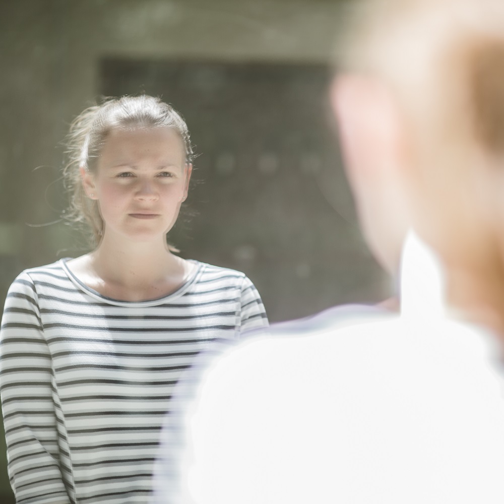 A woman in a striped top standing outside looking at her reflection in a large window.