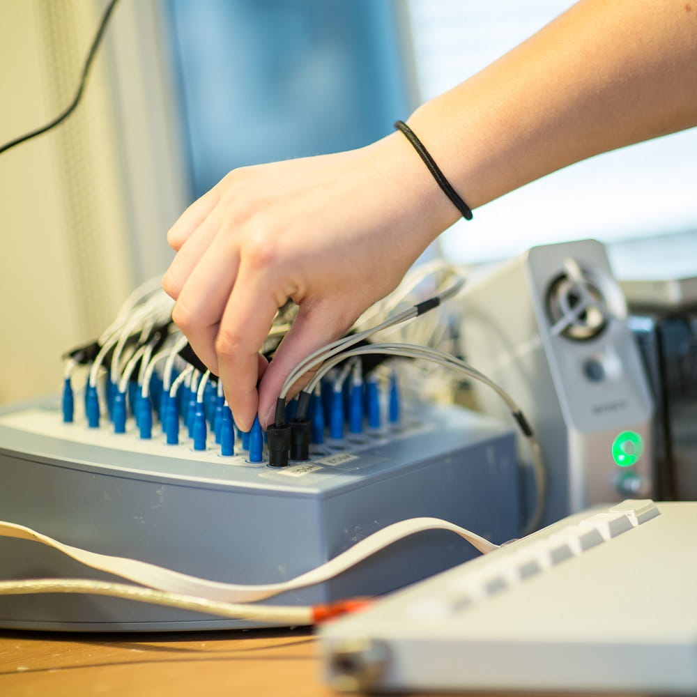 A hand holding a blue jack plug, which is being put in a socket on top of a large metal device. There are multiple rows of jack plugs visible behind the hand.