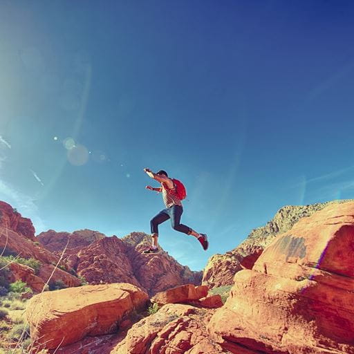 A figure jumping across some orange rocks with a wide blue sky above.