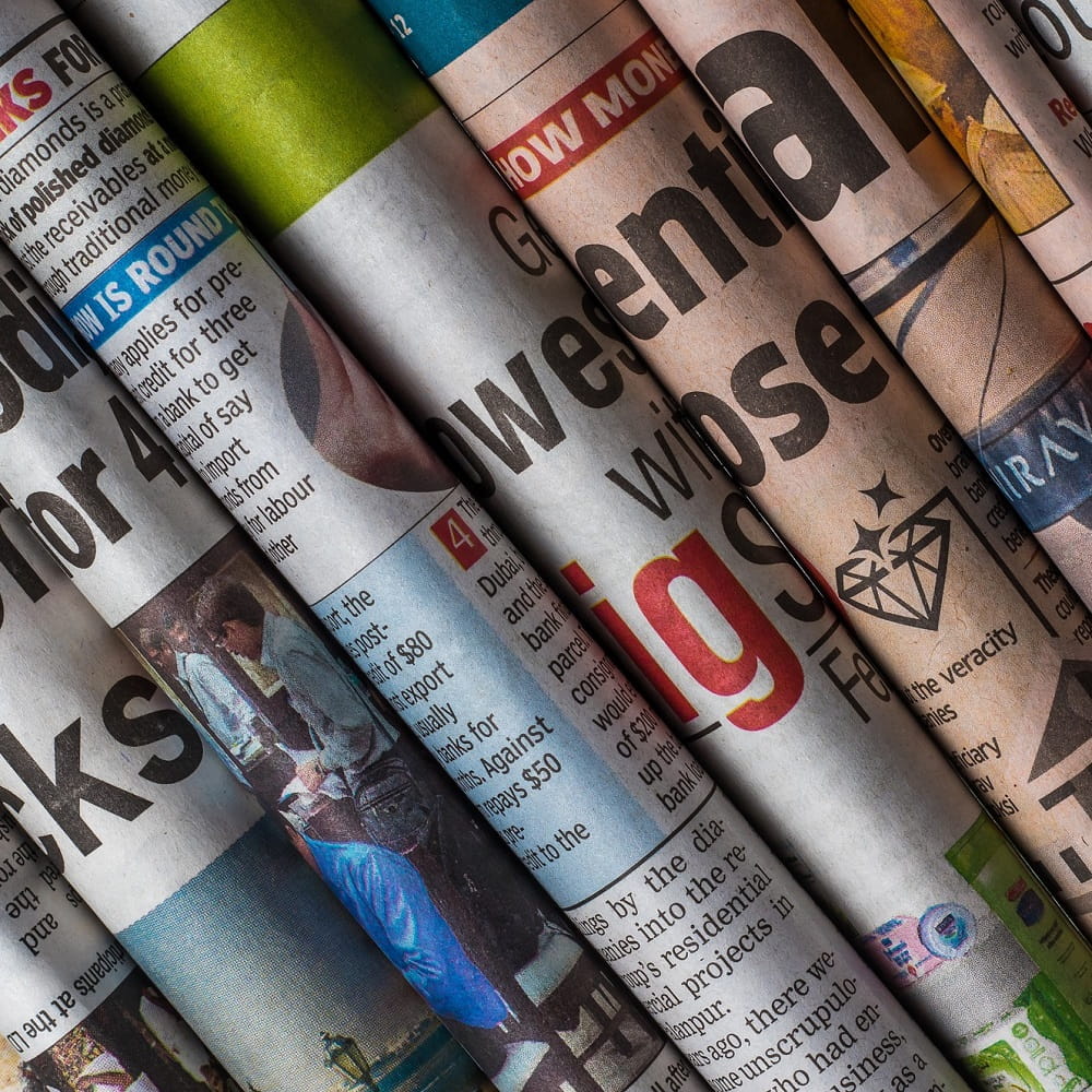 A row of folded newspapers, with only a few letters visible on each one.