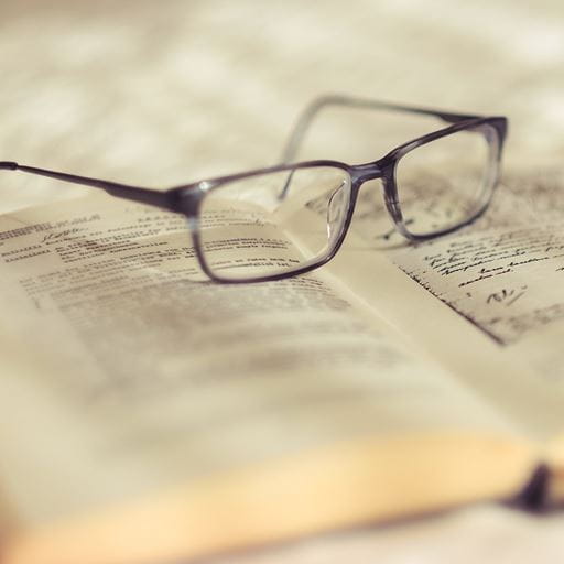 A pair of spectacles resting on the pages of an open book.