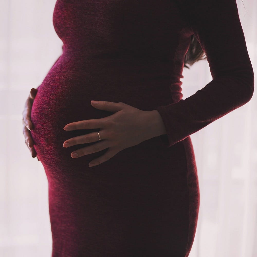 A woman in a red dress, with her head out of shot, standing with her hands on a pregnant bump.