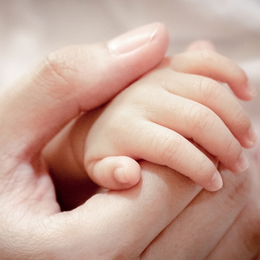 A baby's hand and fingers curling around the hand of an adult.