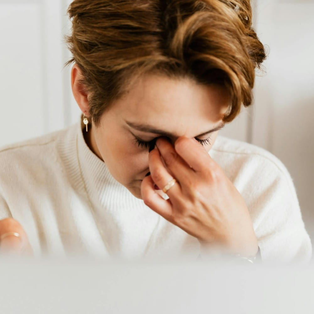 A woman with short hair pinching the bridge of her nose with her eyes closed.