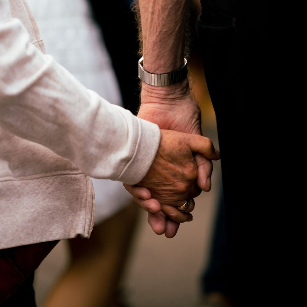 Two people holding hands. One is wearing a watch and the other has long white sleeves covering their arm to their wrist.