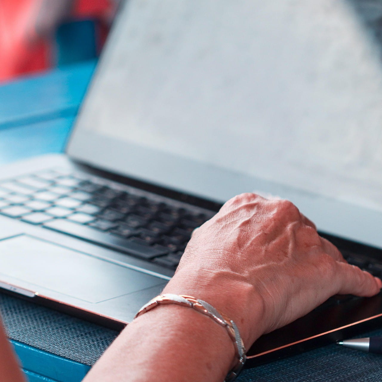 A hand resting on a laptop keyboard. The person is wearing a bracelet on their wrist.