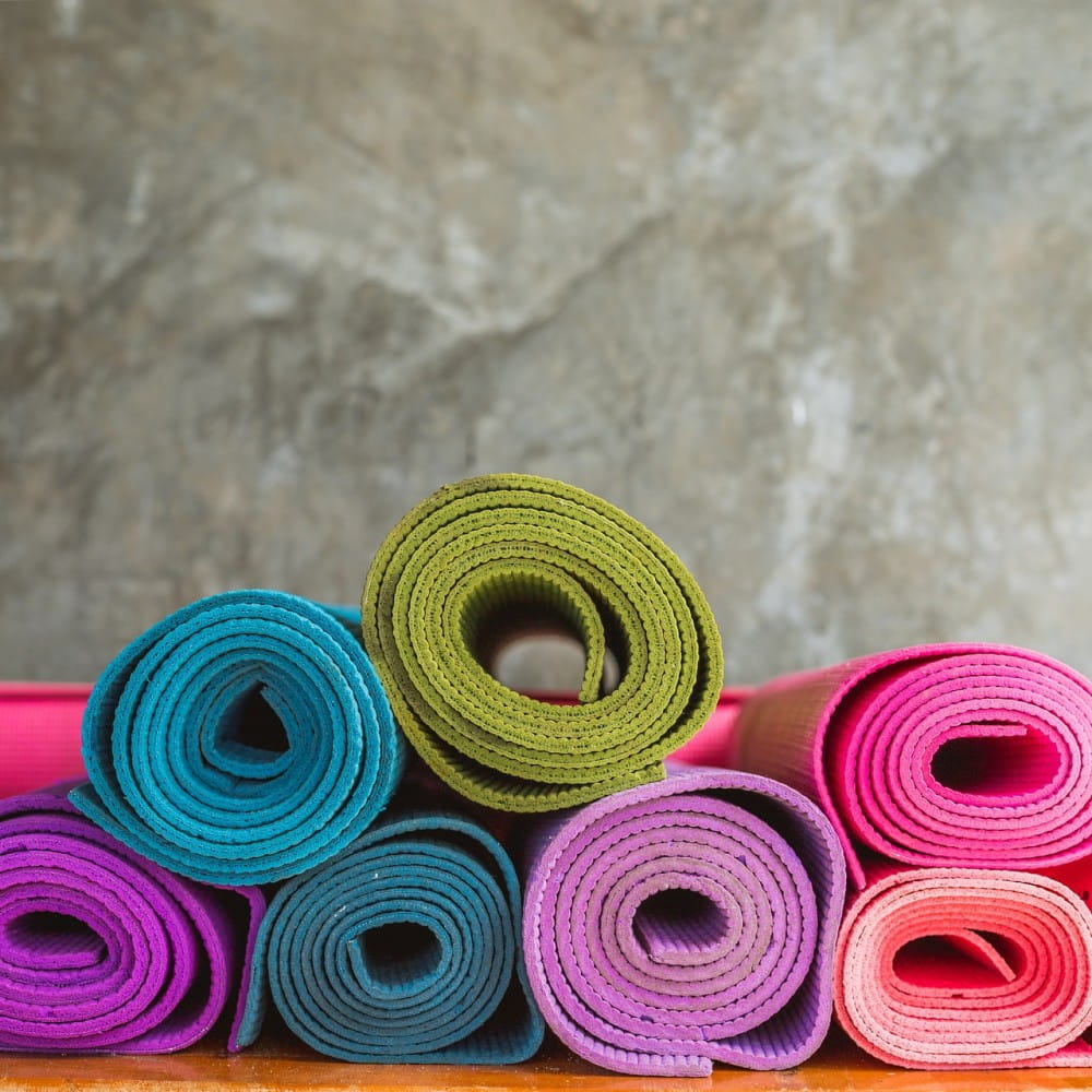Rolled up yoga mats in blue, green, purple and pink, in a small pile.