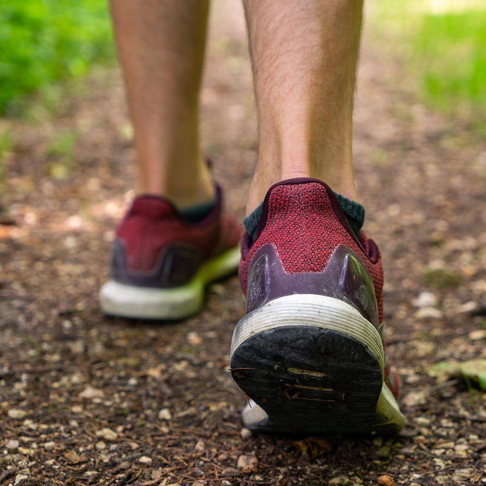 Two feet wearing red and purple trainers. The person is walking away from the camera along a dirt path.