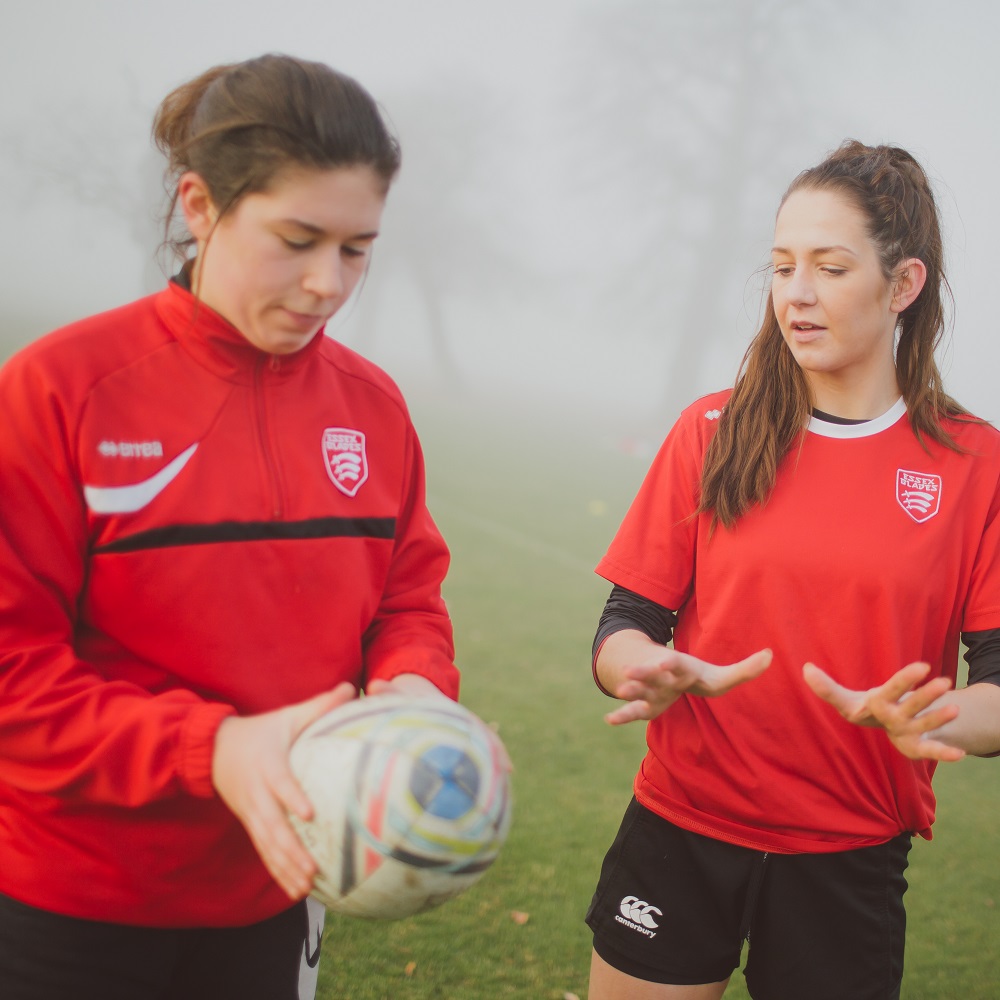 One student coaching another holding a rugby ball