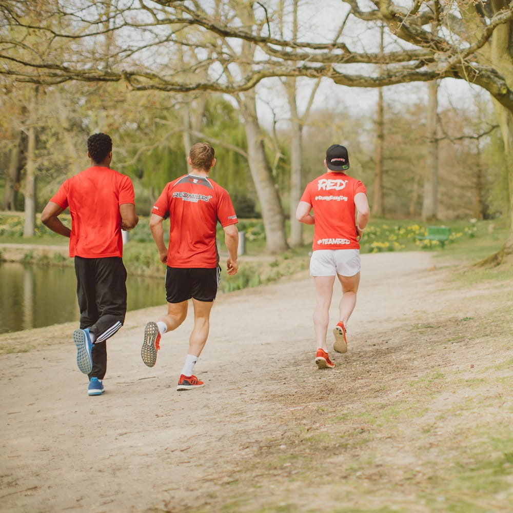 Three men in red t-shirts running along a path