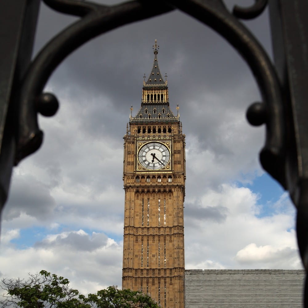Big Ben viewed through an ornate railing, with large grey clouds in the background.