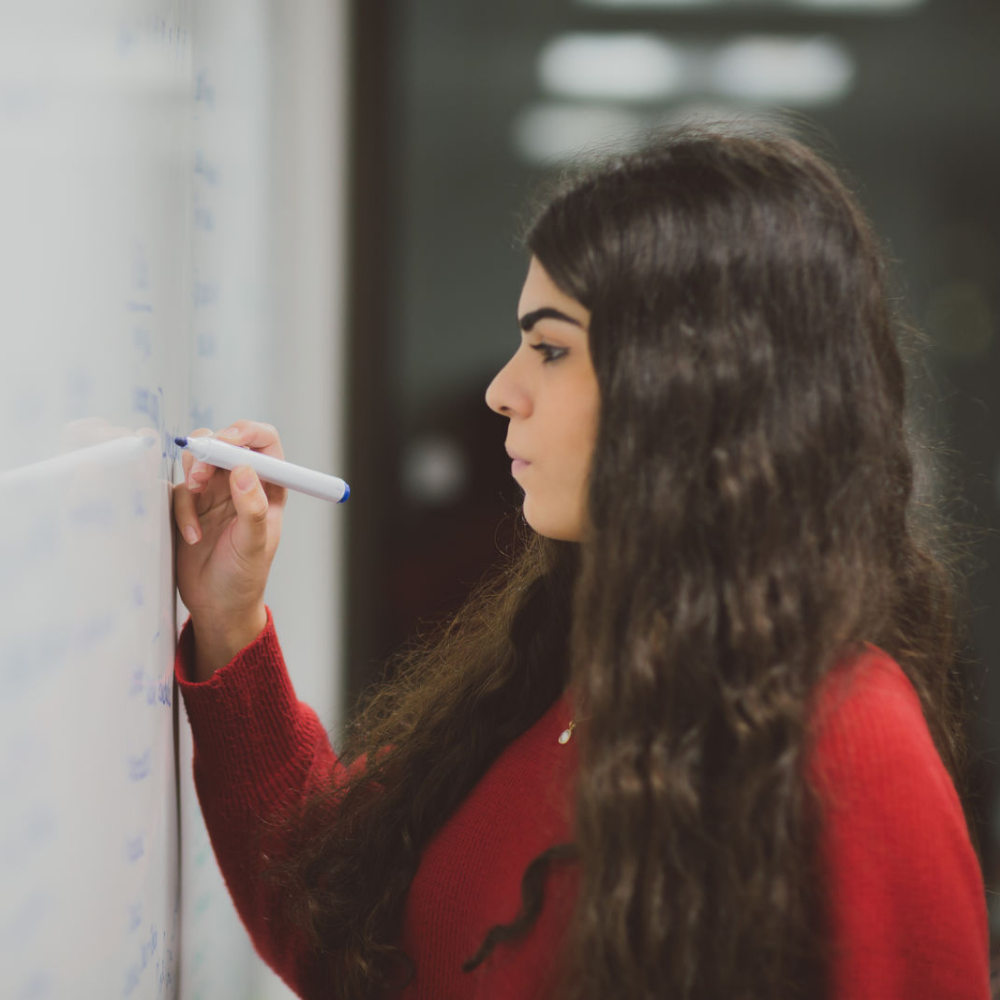 Woman with dark hair writing notes on a whiteboard in a classroom