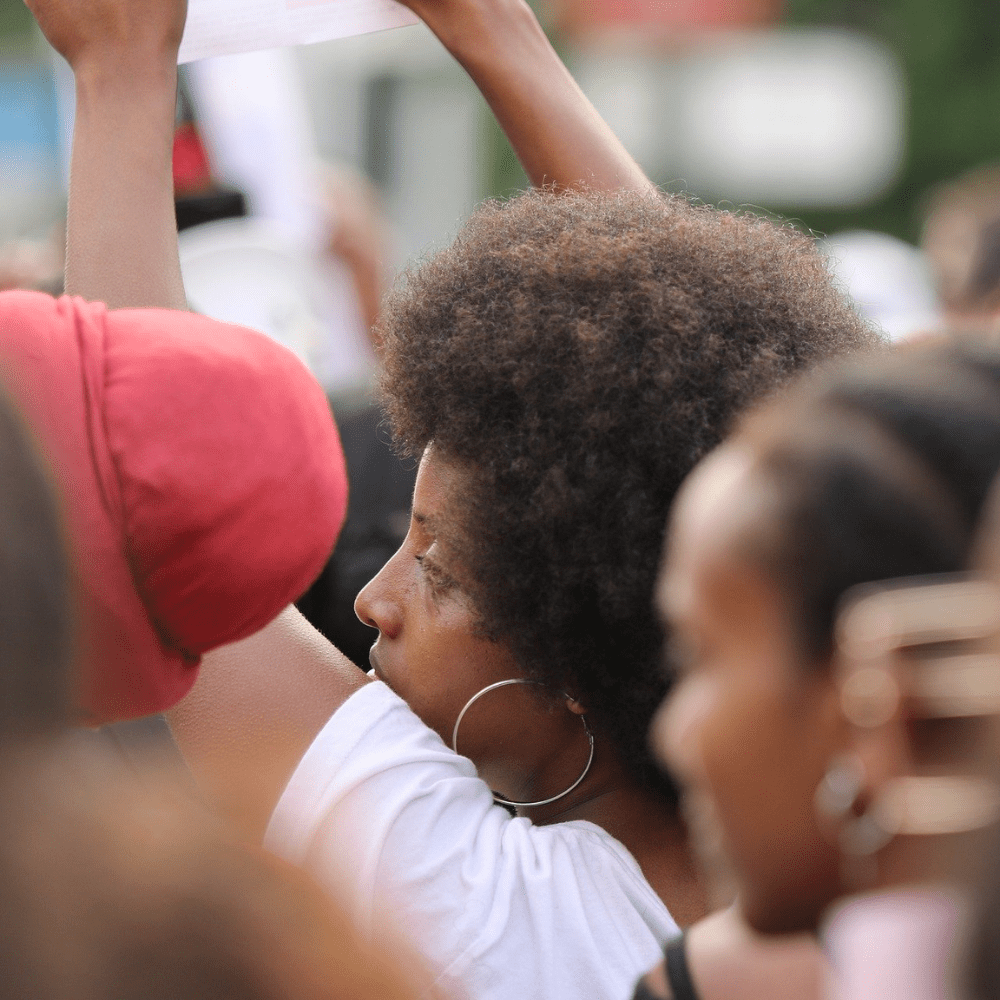 Black female protesters stand shoulder to shoulder at a mass demonstration with their fists raised.