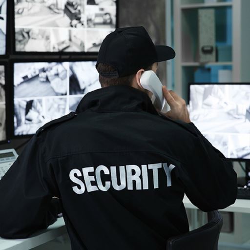 Private security officer holding phone whilst looking at CCTV screens