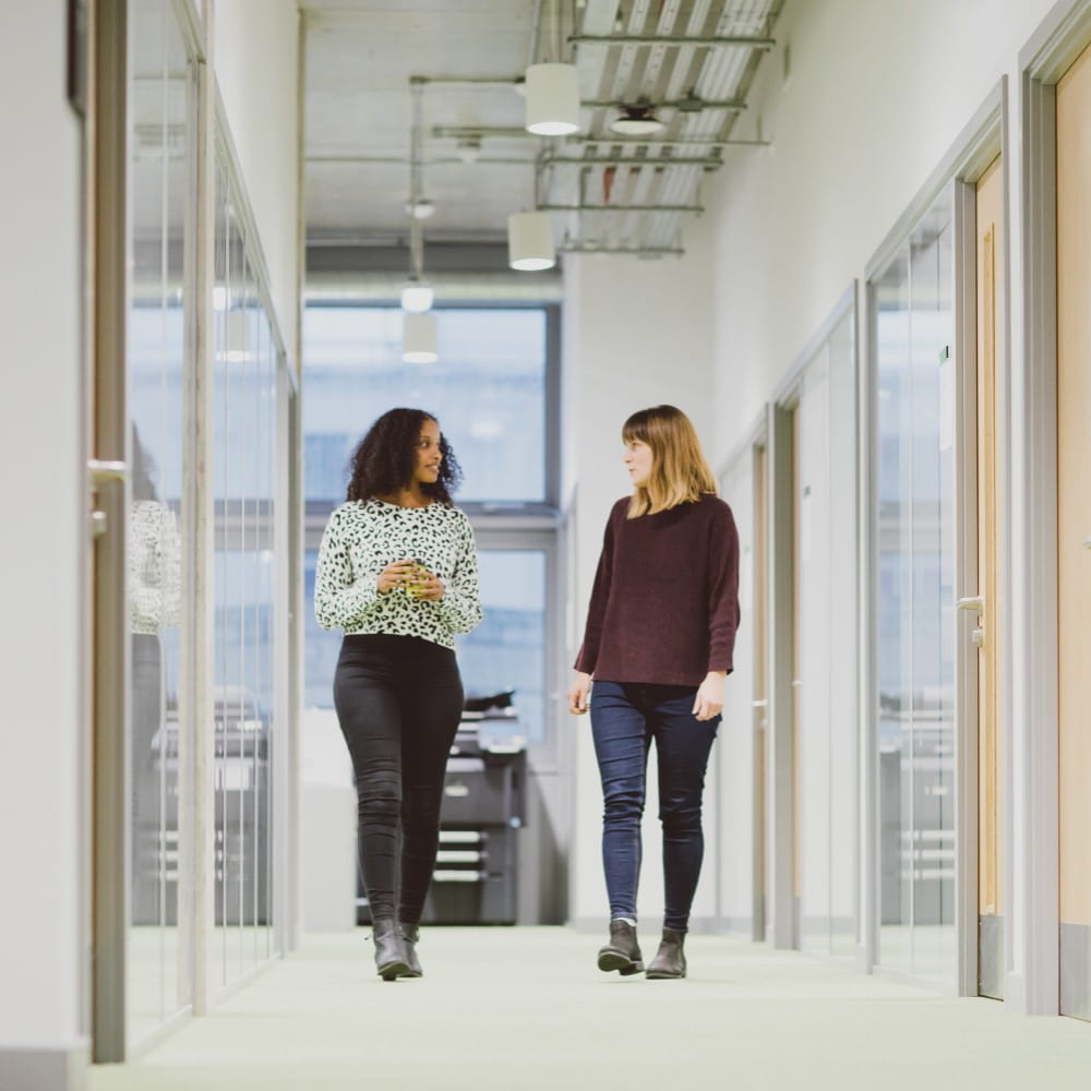 two girls walking along corridor looking at one another