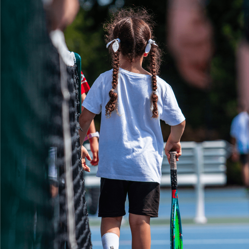Junior kid holding a tennis racket outside on a sunny day - kid walking way holding a tennis racket