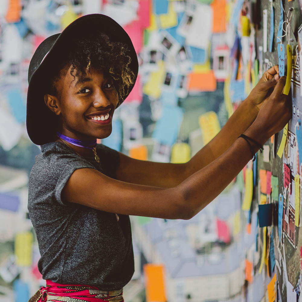 Young woman pinning a note to a wall covered in memos