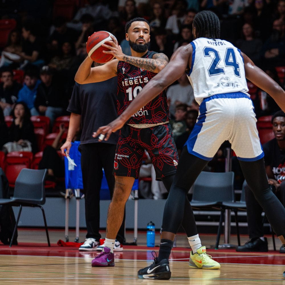 Men's Rebels Basketball player holding ball in front of opposing team player