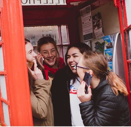 Students laughing holding mobile phones in a red telephone box