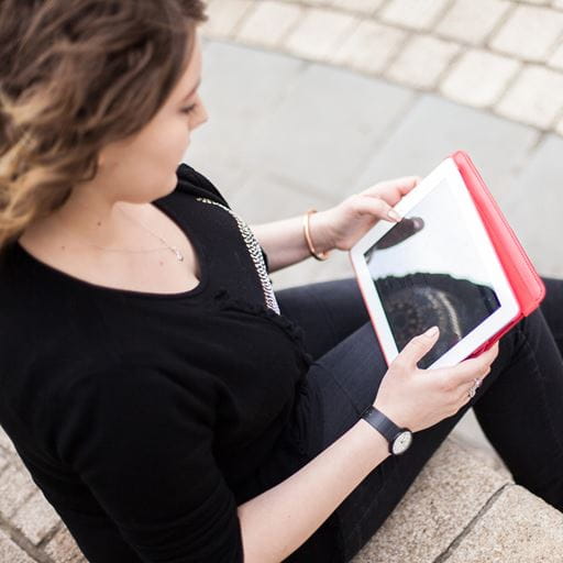 A woman sitting outside, looking at the screen of an ipad.