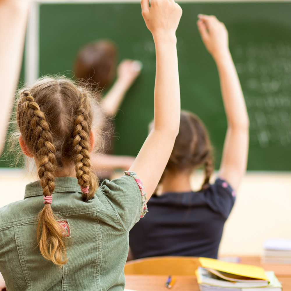 Photo of children in classroom with hands raised