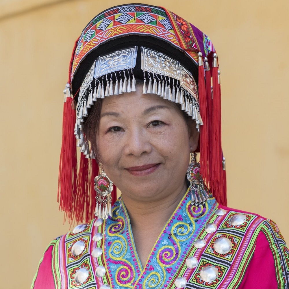 Yuejun, wearing the traditional headdress and outfit of the Red Miao People. The headdress has silver and red tassles.