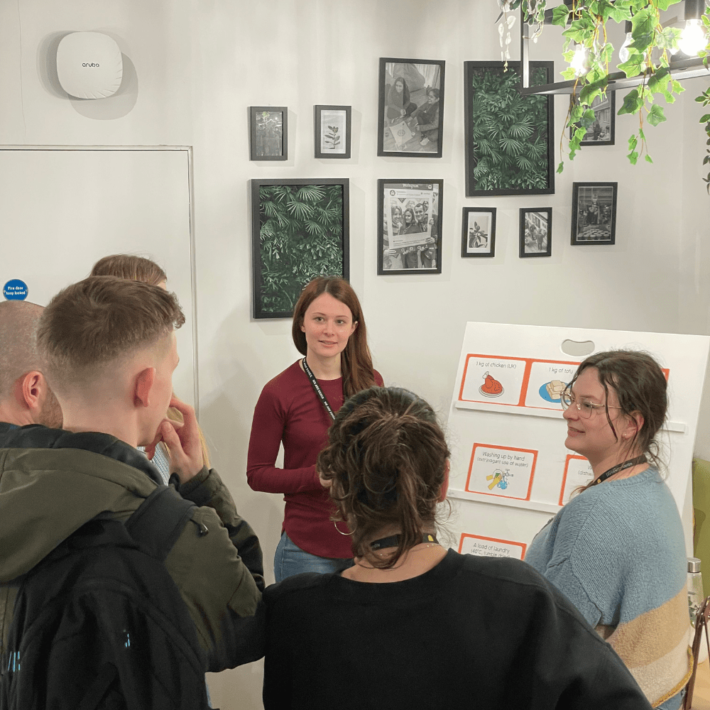 A group of students stand in front of a speaker presenting a carbon footprint game 