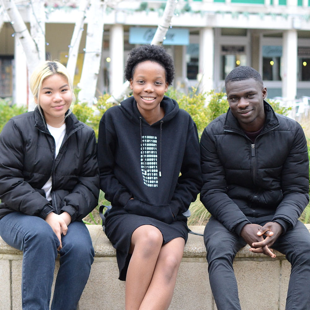 Euphrose, Joseph and Gabby smiling and sitting in the squares at the University of Essex