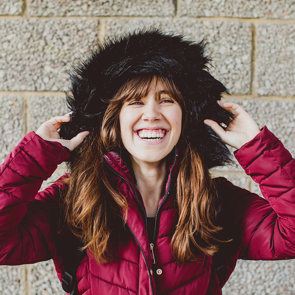 Laura holding the hood of her red puffa jacket and laughing at the camera.
